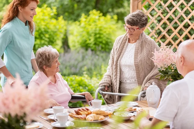 Serene Gathering Outside a One Bedroom Suite with Care Support Outdoor gathering of elderly women with a caretaker enjoying tea and pastries outside a One Bedroom Suite.