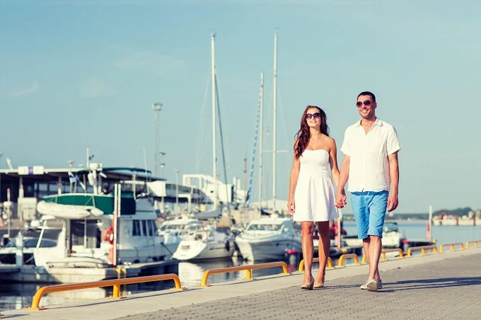 Couple walking near yachts at marina during sailing vacation