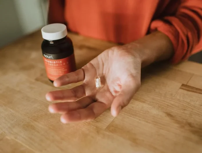 Hand holding a health supplement capsule with a probiotic bottle in the background