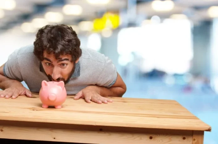 Business owner examining pink piggy bank on wooden desk, demonstrating money-saving techniques for business
