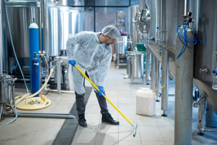 Worker cleaning an industrial conveyor area, ensuring proper maintenance of the conveyor belt cleaner to prevent wear and breakdowns.
